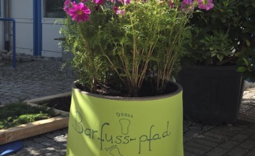 Ein Blumentopf mit angebrachtem Plakat Barfußpfad neben dem angelegten Pfad